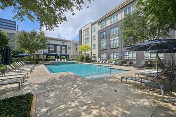 A swimming pool surrounded by lounge chairs and umbrellas in a courtyard at Everra Midtown Park Apartments, Dallas, TX